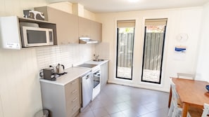 A compact kitchen with white cabinets, a microwave, a kettle, and a sink. - ALLAMBIE COTTAGES - VILLA 2: Bright (Bright)