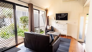 A modern living room with a sofa, a television, and a view of a garden through large windows.