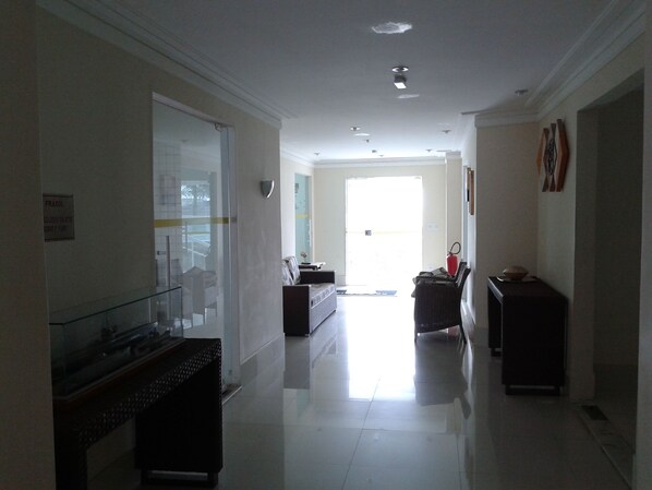 A hotel corridor with a glass door, a reception desk, and a fire extinguisher. - BEAUTIFUL APARTMENT FACING THE SEA (Praia Grande)