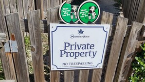 Cerca de madeira com uma placa de 'Propriedade Privada' e duas placas com a inscrição 'Limpe após seu animal de estimação'.