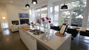 A modern kitchen with a central island, stainless steel sink, and a dining area with a wooden table and chairs. - Barwon Heads beach and river - great location. Flexible cancellation (Barwon Heads)