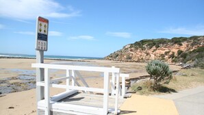 A beach with a wooden walkway leading to a white gate, a rocky cliff in the background, and a clear blue sky. - Barwon Heads beach and river - great location. Flexible cancellation (Barwon Heads)