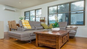 A modern living room with a grey sectional sofa, a wooden coffee table, and a view of the outdoors through large windows.