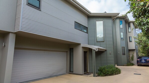 A modern two-story residential building with a garage, a covered entryway, and a small front yard.