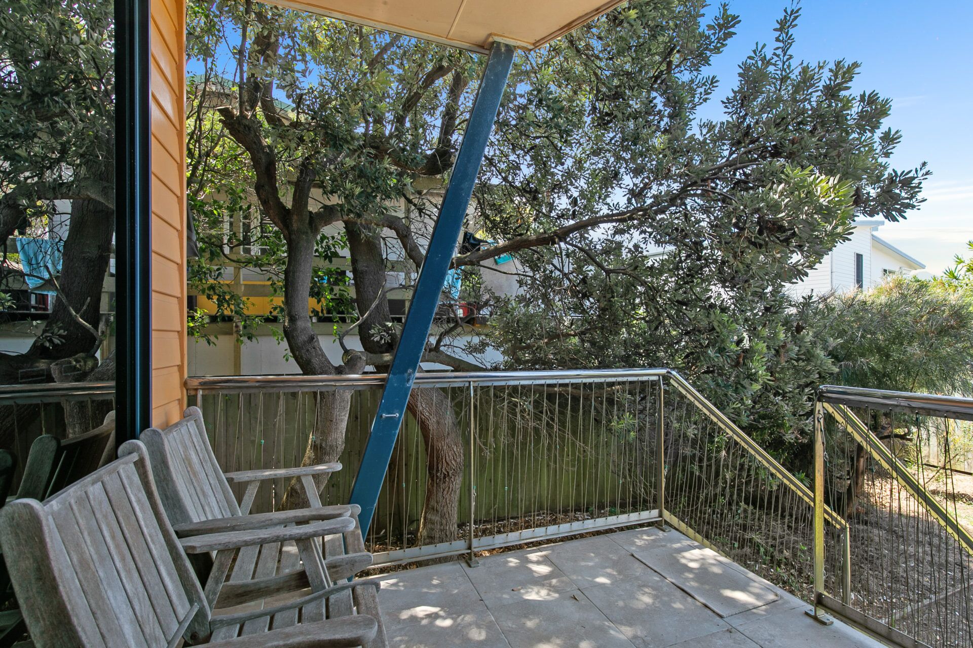 A covered outdoor seating area with wooden benches, a metal railing, and trees in the background.