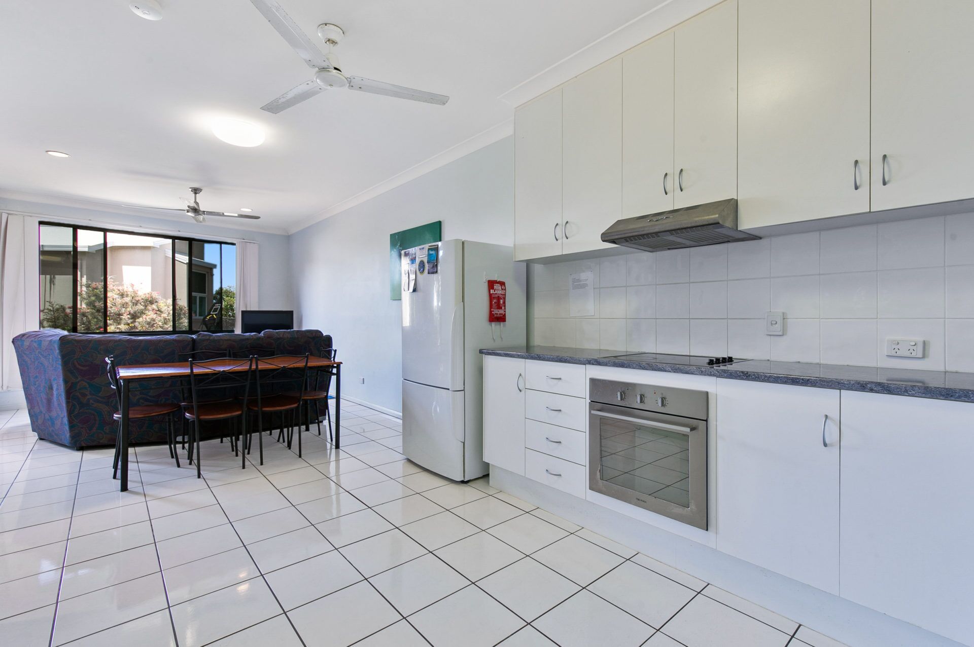 A modern kitchen with white cabinets, a built-in oven, and a dining area with a sofa and table.