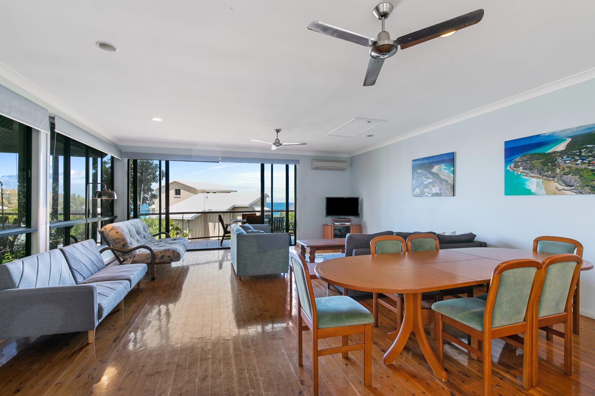 A spacious living room with a large dining table, comfortable seating, and a balcony with a view of the ocean.