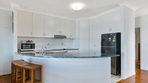 A modern kitchen with white cabinets, a stainless steel refrigerator, a built-in microwave, and a granite countertop island with bar stools.