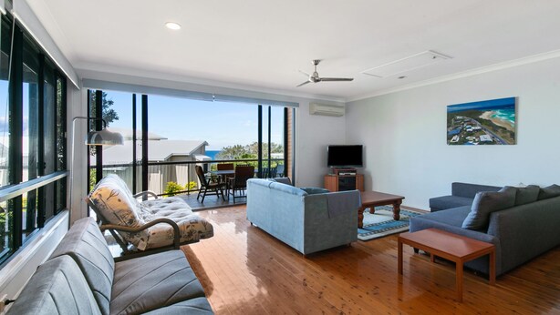 A spacious living room with a large window, a ceiling fan, and a flat-screen TV.
