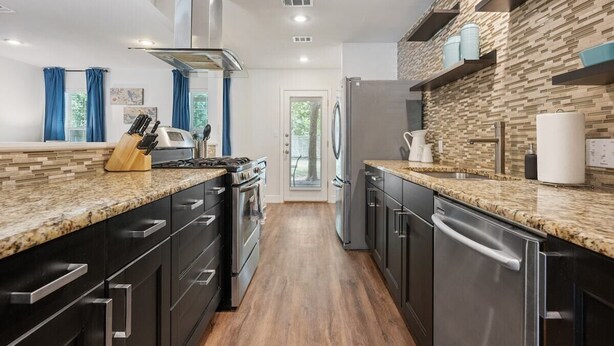 Une cuisine moderne dotée de plans de travail en granit, d’appareils électroménagers en acier inoxydable et d’un pare-feu en bois disposé en motif chevrons.