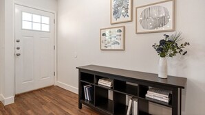Un couloir avec une porte blanche, une console noire sur laquelle sont posés des livres, et trois œuvres d’art encadrées accrochées au mur.