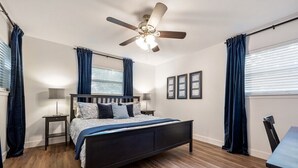 Une chambre à coucher avec un lit, un ventilateur de plafond, une table de chevet et une fenêtre avec des rideaux.