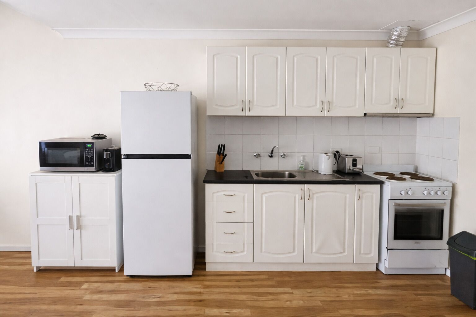 A compact kitchen with white cabinets, a microwave, a refrigerator, a sink, and a stove.