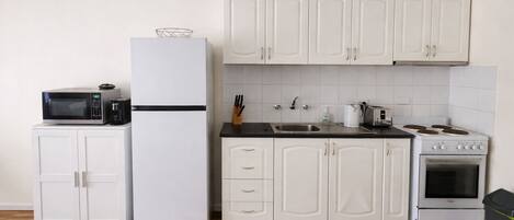 A compact kitchen with white cabinets, a microwave, a refrigerator, a sink, and a stove.