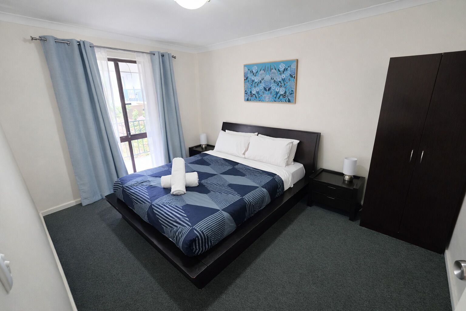 Ein modernes Hotelzimmer mit Bett, Nachttisch, Schrank und einem Bild an der Wand.