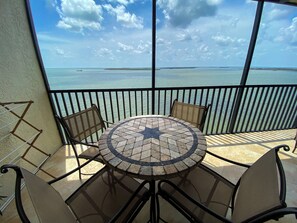 A balcony with a round table and chairs, overlooking a body of water.