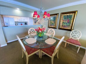 A dining area with a glass table, red upholstered chairs, a chandelier, and framed artwork on the wall.