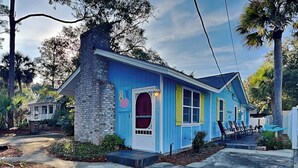 A two-story house with a blue exterior, a brick chimney, and a front porch with chairs. - Charming Tybee home w. patio, grill + pet friendly! (Tybee Island)