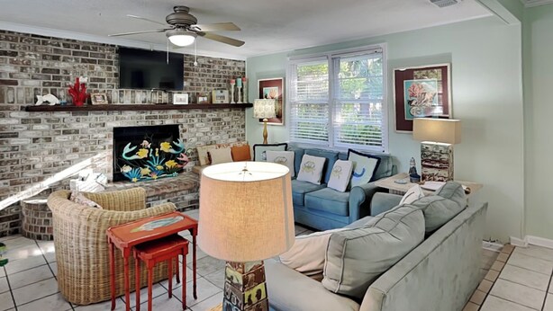 A living room with a brick fireplace, a ceiling fan, a television, and a blue sofa. - Charming Tybee home w. patio, grill + pet friendly! (Tybee Island)