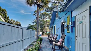 A narrow pathway with a row of rocking chairs on one side and a white door on the other. - Charming Tybee home w. patio, grill + pet friendly! (Tybee Island)