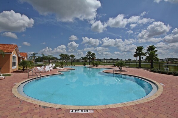 Relax by the clear pool surrounded by a brick walkway and lounge chairs.
