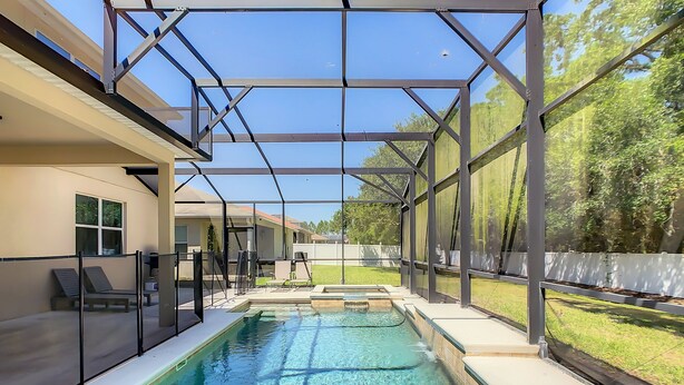 En swimmingpool med en glasvägg runt om, en täckt uteplats och utsikt över ett bostadsområde.