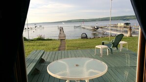A deck with a glass-top table and chairs, overlooking a lake with boats and a dock.