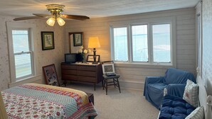 A bedroom with a bed, a chair, a dresser, a ceiling fan, and a window with blinds.