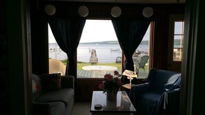 A room with a view of a lake, a wooden deck, and outdoor furniture.