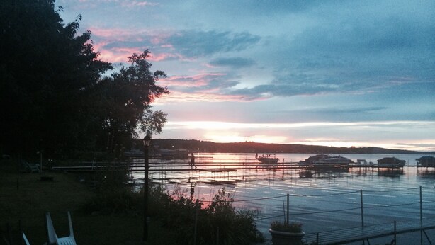 A lakeside view with boats, a dock, and a chair by the water.