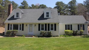 A two-story house with a gabled roof, a front porch, and a chimney. - Designer Home in Mashpee with central A/C (Mashpee)
