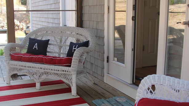 A porch with a white wicker chair and a red and white striped rug. - Designer Home in Mashpee with central A/C (Mashpee)