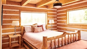 Un dormitorio tipo cabaña de madera con una cama de madera, dos lámparas de noche y un ventanal grande.