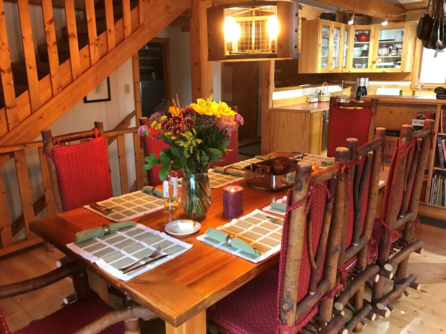 Ein Holzespeisetisch, gedeckt mit einem Blumenstrauß, Kerzen und einem Braten in einer Pfanne.
