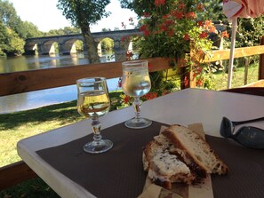 A table with two wine glasses and a sandwich, overlooking a river with a bridge in the background. - Romantic Stone Cottage at 2 km from celebrated Castles and the Dordogne River (Veyrines-De-Domme)