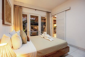 A bedroom with a bed, pillows, a bedside lamp, and a view of an outdoor area with a dining table and chairs.