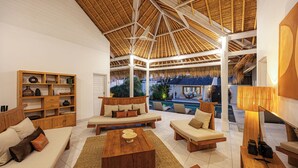 Un'ampia zona giorno con soffitto alto, arredi in legno, piscina e vista sull'esterno.