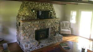 A stone fireplace with a television on top, a chair, and a wooden table with books. - Shawano WI Wolf River home with lake access via Shawano Lake Channel (Shawano)