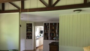 A spacious living room with a wooden floor, a green armchair, and a beige sofa with colorful cushions. A kitchen is visible in the background with wooden cabinets and a dining area. - Shawano WI Wolf River home with lake access via Shawano Lake Channel (Shawano)