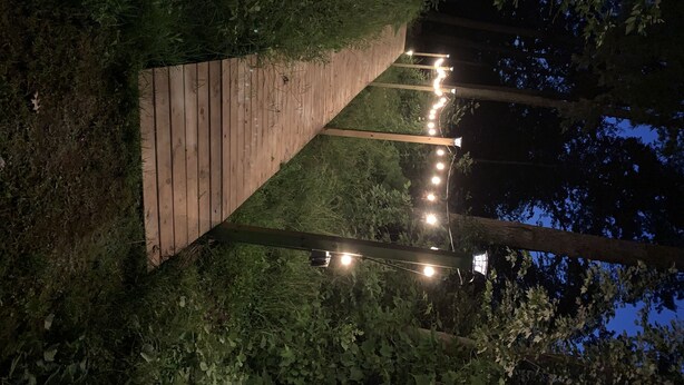 A wooden pathway leading through a wooded area with string lights along the path. - Shawano WI Wolf River home with lake access via Shawano Lake Channel (Shawano)