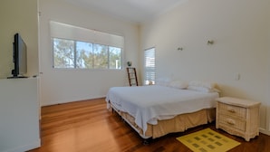 A bedroom with a bed, a wooden floor, a window, a bedside table, and a television. - Watson Street 1, 29, Currimundi (Currimundi)