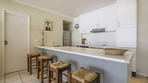 A modern kitchen with white cabinets, a stainless steel refrigerator, a sink, and a bar area with stools. - Watson Street 1, 29, Currimundi (Currimundi)