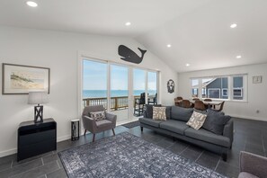 A living room with a gray sofa, a small armchair, a coffee table, a lamp, and a rug. There is a large window with a view of the ocean. - 449 Ocean-Front Amazing Views & Easy Beach Access (Nags Head)