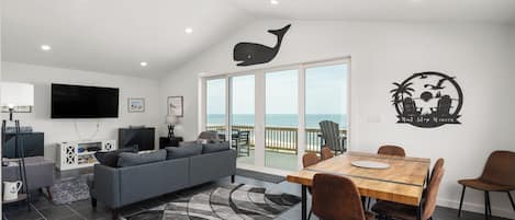Una sala de estar moderna con sofá, televisor y comedor con sillas y mesa.