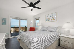 A bedroom with a bed, a nightstand, a lamp, a ceiling fan, a window with a view, and a framed picture on the wall. - 449 Ocean-Front Amazing Views & Easy Beach Access (Nags Head)