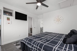 Quarto com cama, ventilador de teto, TV na parede, calendário e decoração de parede com bússola.