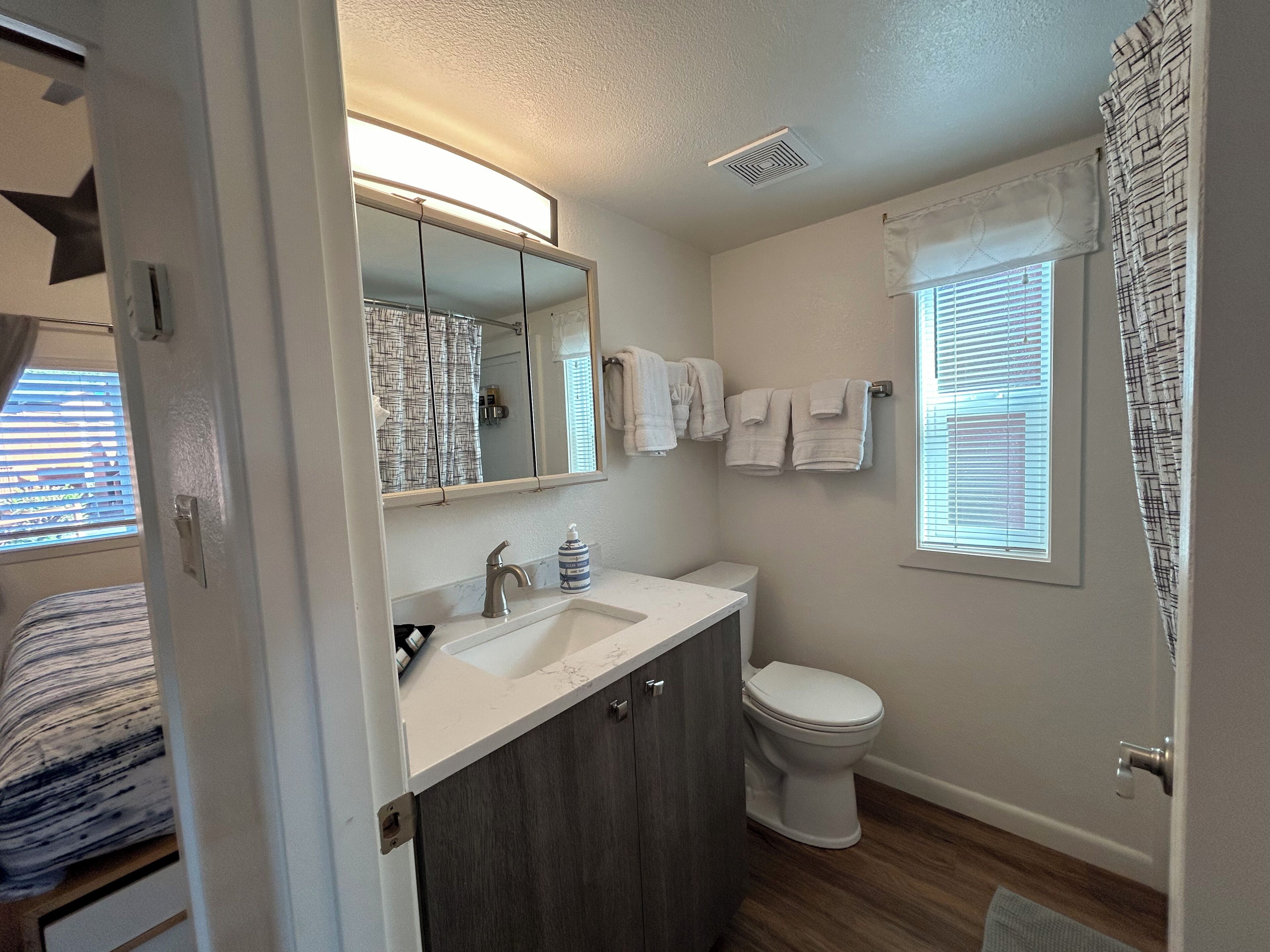 A bathroom with a white sink, a mirror, a toilet, and a window with blinds.