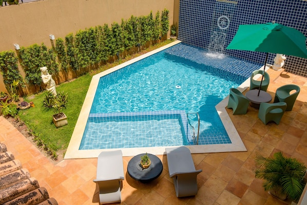 Une piscine dont le bord est revêtu de carrelage, entourée d’une terrasse aménagée avec des chaises longues et une petite table.