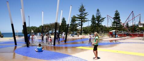 A water play area with multiple water jets and a sandy surface.