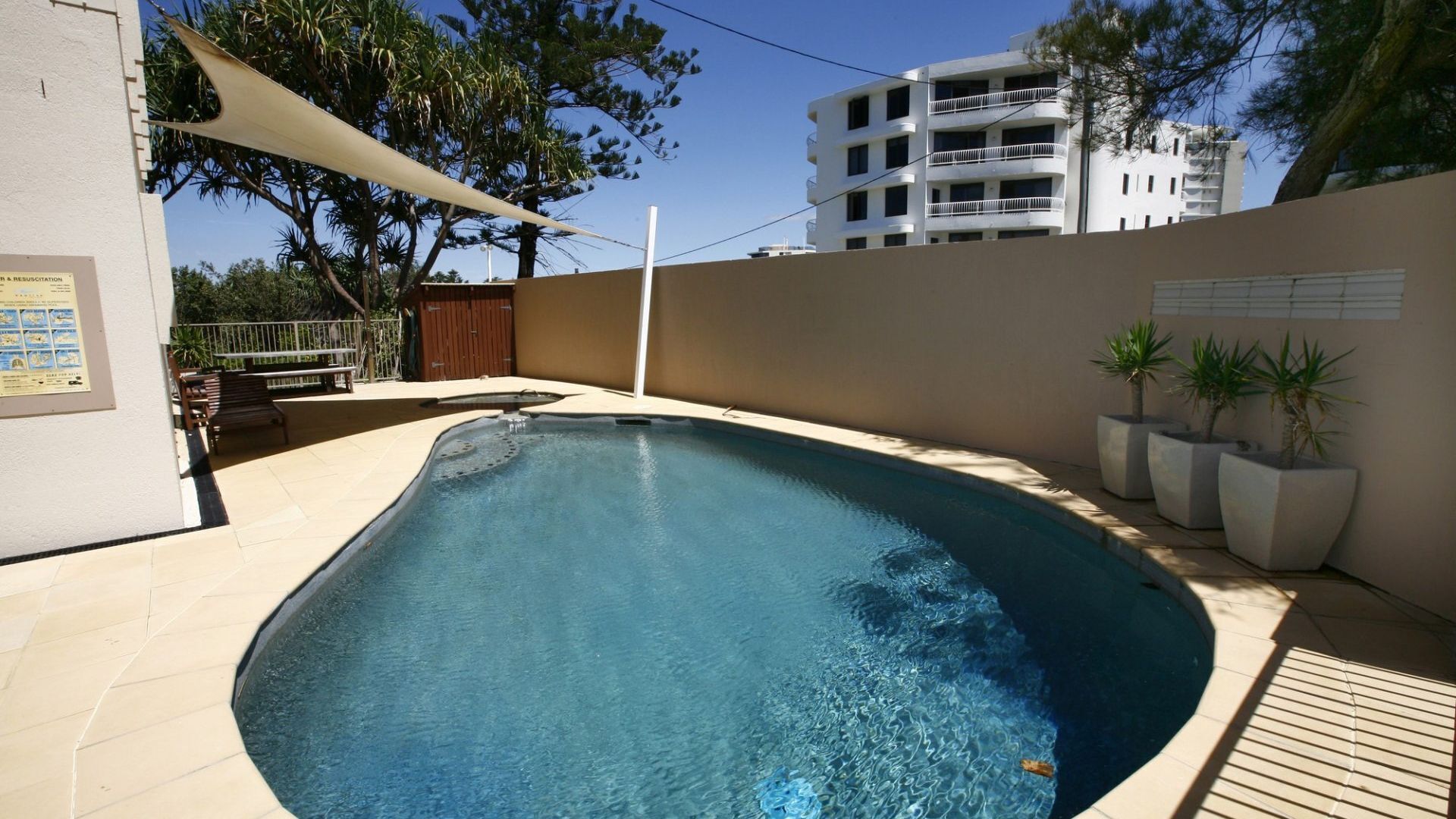 A swimming pool with a tiled deck, surrounded by a low wall and potted plants.
